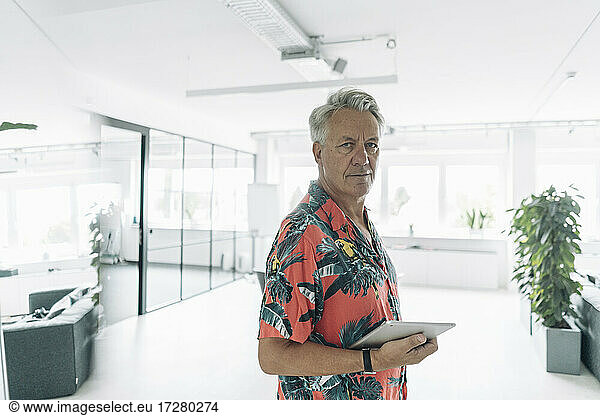 Geschäftsmann in Freizeitkleidung  der ein digitales Tablet hält  während er im Büro steht