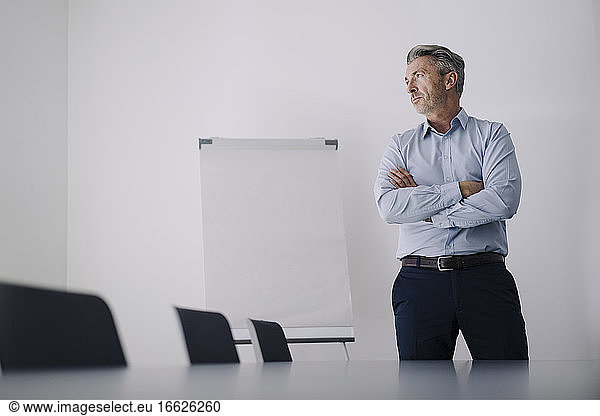 Geschäftsmann mit verschränkten Armen im Sitzungssaal im Büro stehend