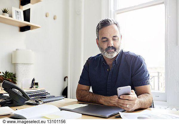 Geschäftsmann nutzt Smartphone  während er am Schreibtisch im Kreativbüro sitzt