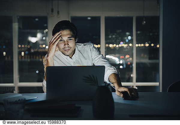 Geschäftsmann schaut auf Laptop  während er bis spät in dunkler kreativer Umgebung arbeitet