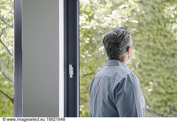 Geschäftsmann schaut durch ein Fenster  während er im Büro steht