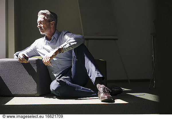 Geschäftsmann sitzt mit einem Hocker auf dem Boden im Büro