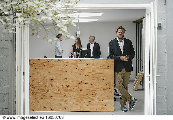 Geschäftsmann steht in offener Bürotür  Menschen arbeiten im Hintergrund