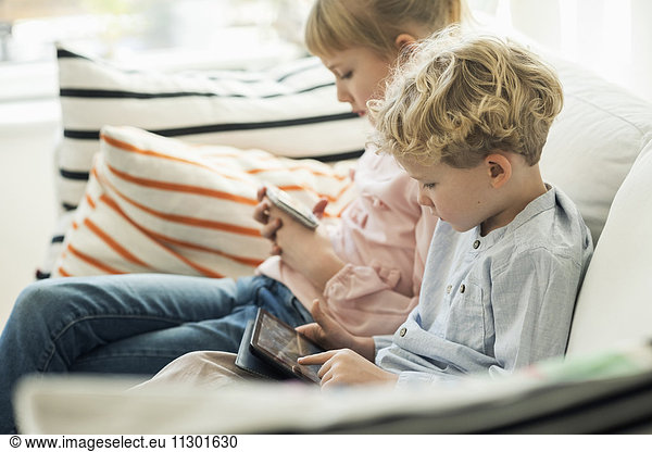 Geschwister mit Technologien auf dem Sofa zu Hause