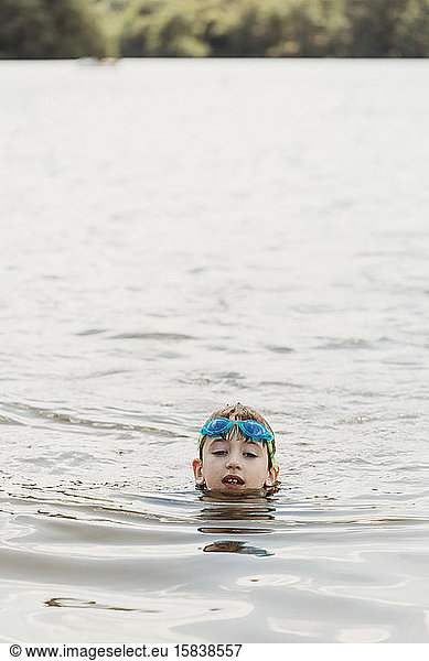 Gesicht eines Jungen mit Schutzbrille im Wasser mit dahinter liegender Uferlinie