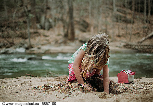 gesichtsloses Porträt eines jungen Mädchens am Flussufer beim Spielen im Sand