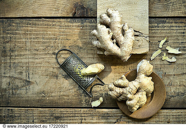 Ginger roots and old grater lying on wooden surface