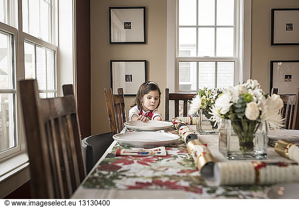 Girl adjusting plate on dining table at home during Christmas