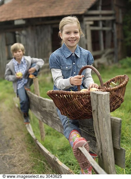 Girl and boy on fence with apples