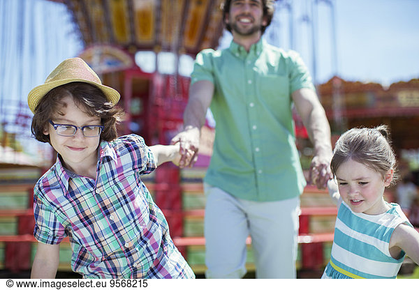 Girl and boy pulling their father in amusement park