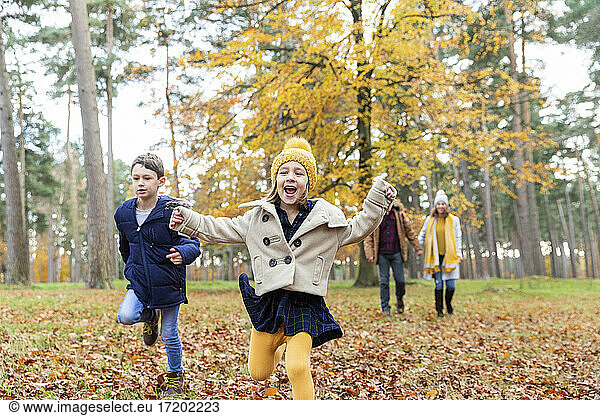 Girl and boy running while playing with parents walking in background at forest