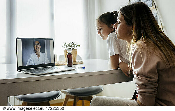 Girl and woman listening to female pediatrician on video call through laptop at home