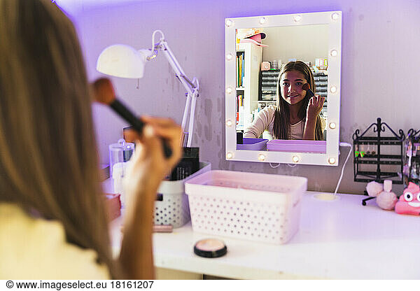 Girl applying make-up with brush looking in mirror at home