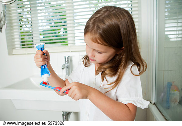 Girl applying toothpaste to brush in bathroom