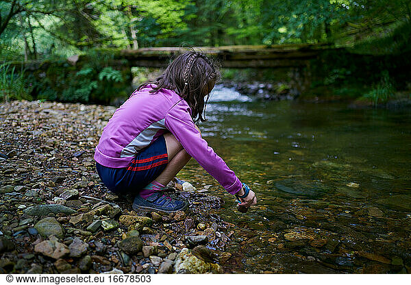 girl bending over a river bank playing with water and stones