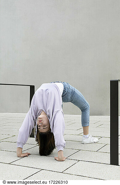 Girl bending over backwards by wall