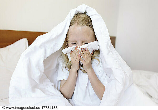 Girl blowing nose with tissue at home