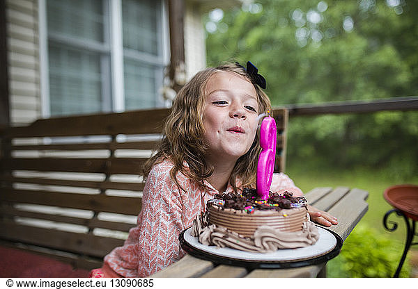 Girl blowing out number 6 candle on birthday cake at porch