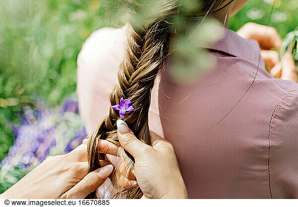Girl braids a flower in a braid on nature
