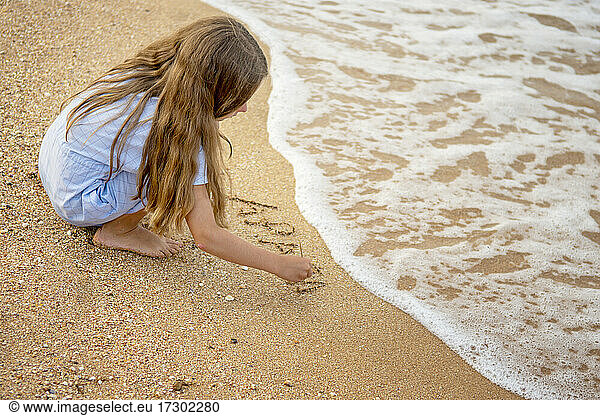 Girl by the sea on the beach writes letters on the sand