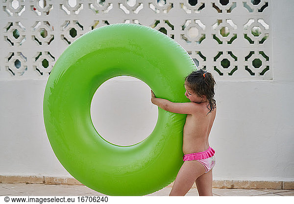 girl carries a green float in her arms by the pool