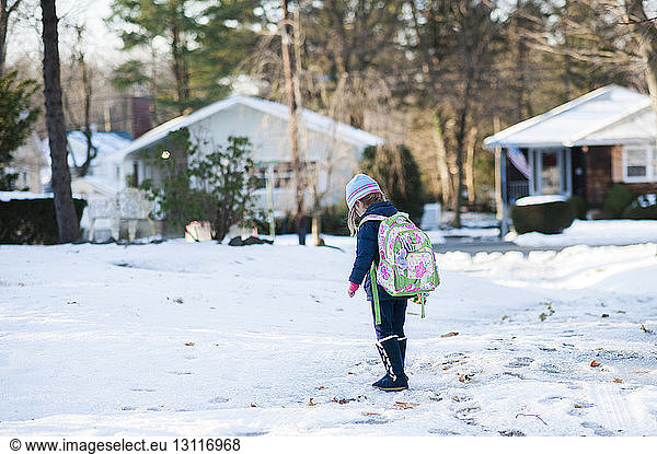 Girl carrying backpack walking on snowy field