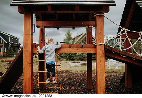 Girl climbing ladder to playground platform  rear view