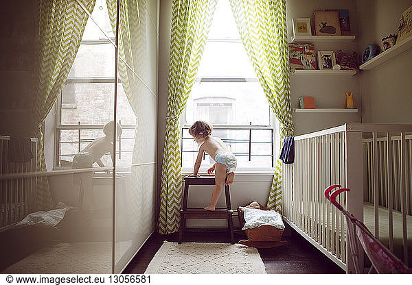 Girl climbing stool by window at home