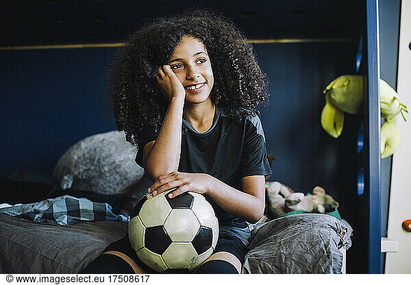 Girl contemplating with soccer ball in bedroom