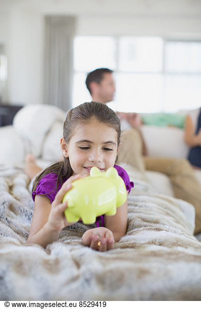 Girl counting change in piggy bank on sofa in living room
