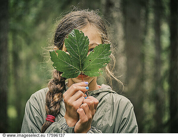 Girl covering face with green maple leaf