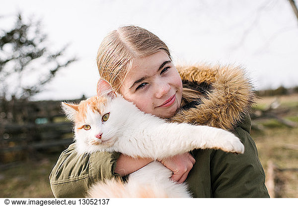 Girl cuddling cat in field