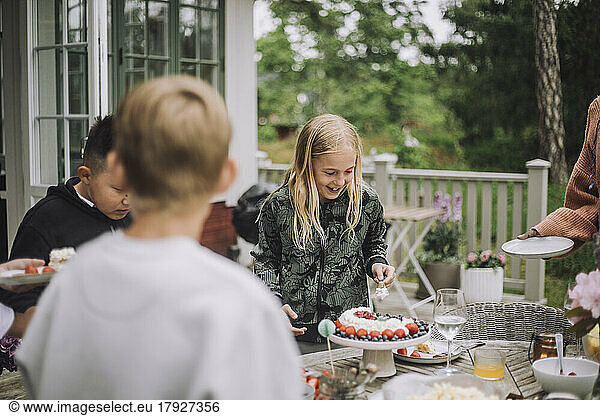 Girl cutting birthday cake while standing near table