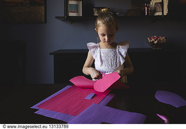 Girl cutting craft papers on table at home