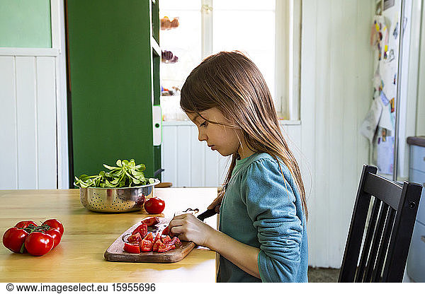 Girl cutting tomatoes on chopping board in kitchen