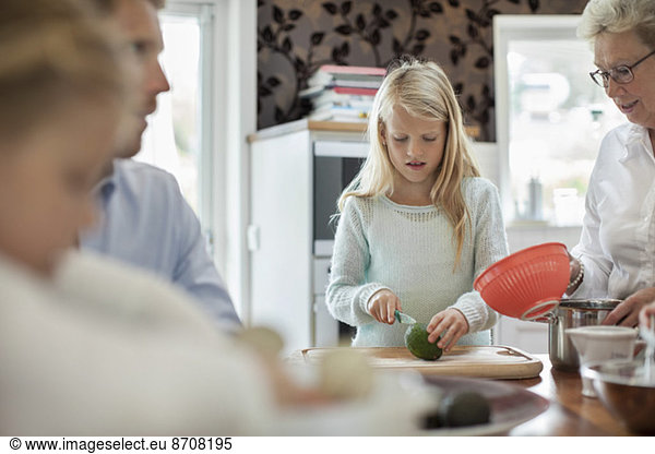 Girl cutting vegetables while cooking food with family in kitchen