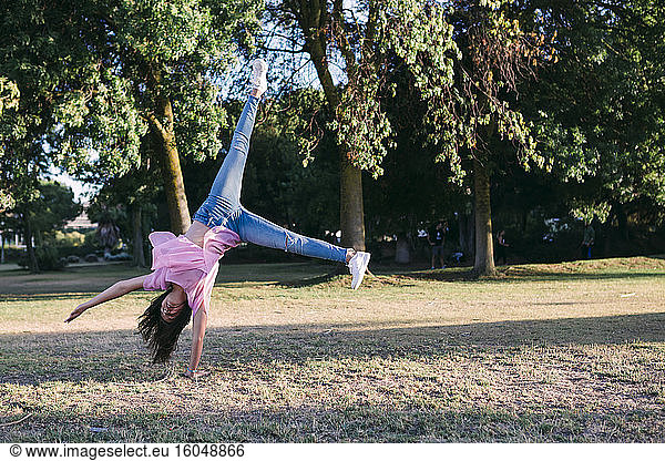 Girl doing cartwheel on land against trees in park