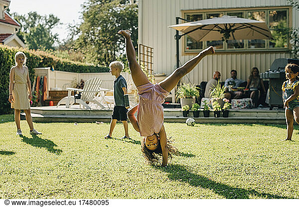 Girl doing cartwheel while playing with friends in backyard on sunny day