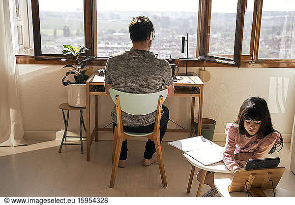 Girl doing homework while her father working on laptop in the background
