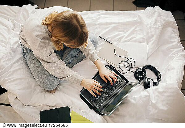Girl doing homework while using laptop in bedroom at home