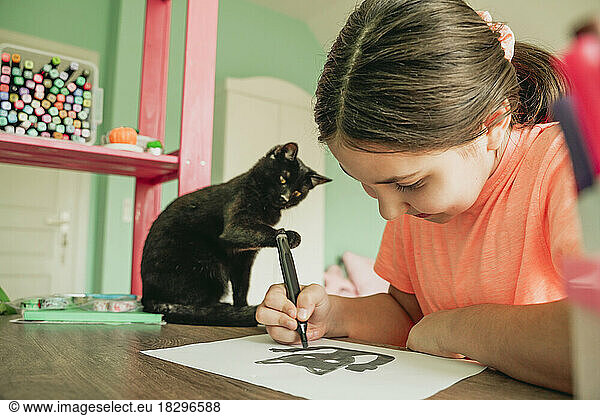 Girl drawing cat picture on paper at home