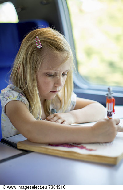 Girl drawing pictures while sitting on train's seat