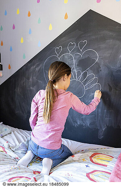 Girl drawing with chalk on board in bedroom at home