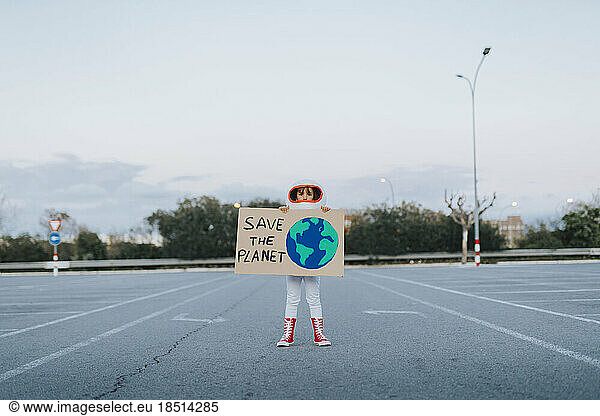Girl dressed as astronaut showing Save The Planet cut out standing in parking lot