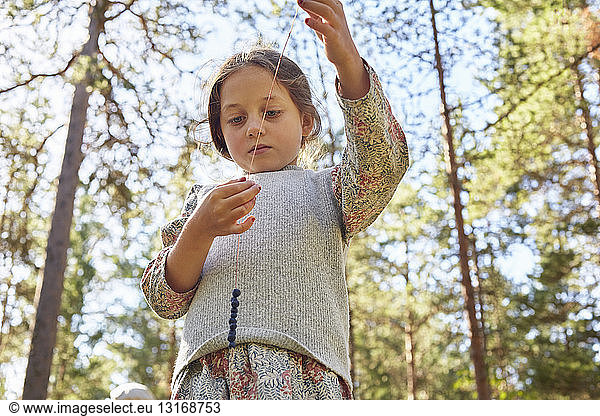 Girl dressed in retro clothing threading berries in forest