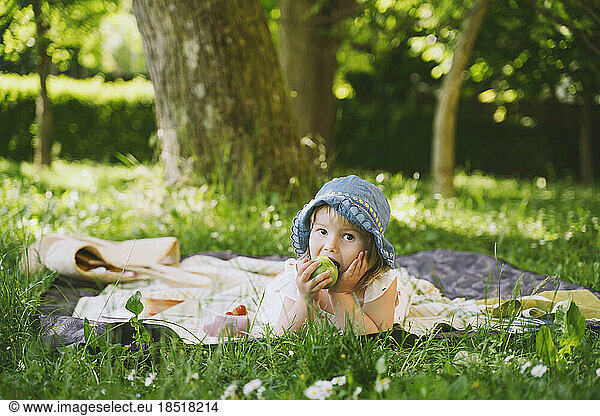 Girl eating green apple lying on grass in garden