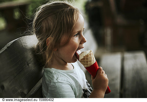 Girl eating ice cream sitting on bench