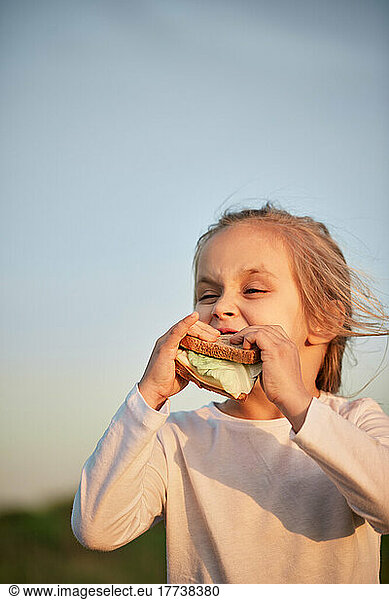 Girl eating sandwich in front of sunset sky