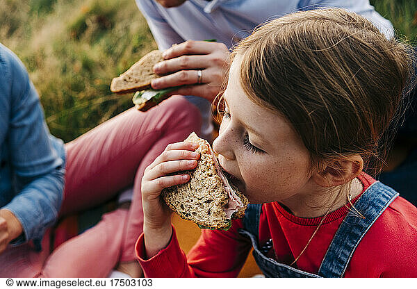 Girl eating sandwich with parents at park