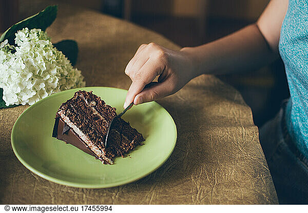 Girl eats chocolate cake at table with hydrangea